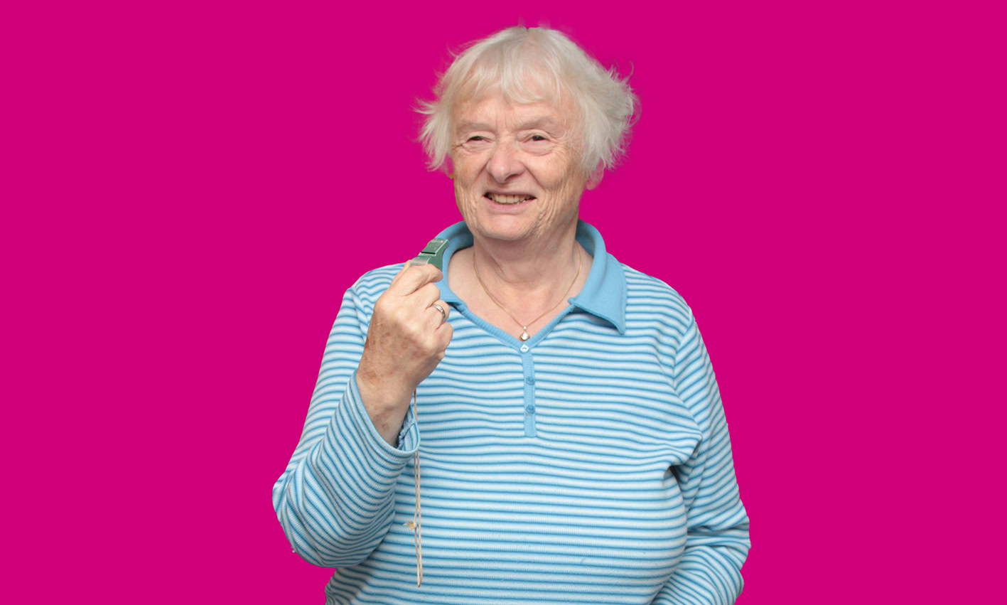 Ältere Dame mit Trillerpfeife vor pinkem Hintergrund.