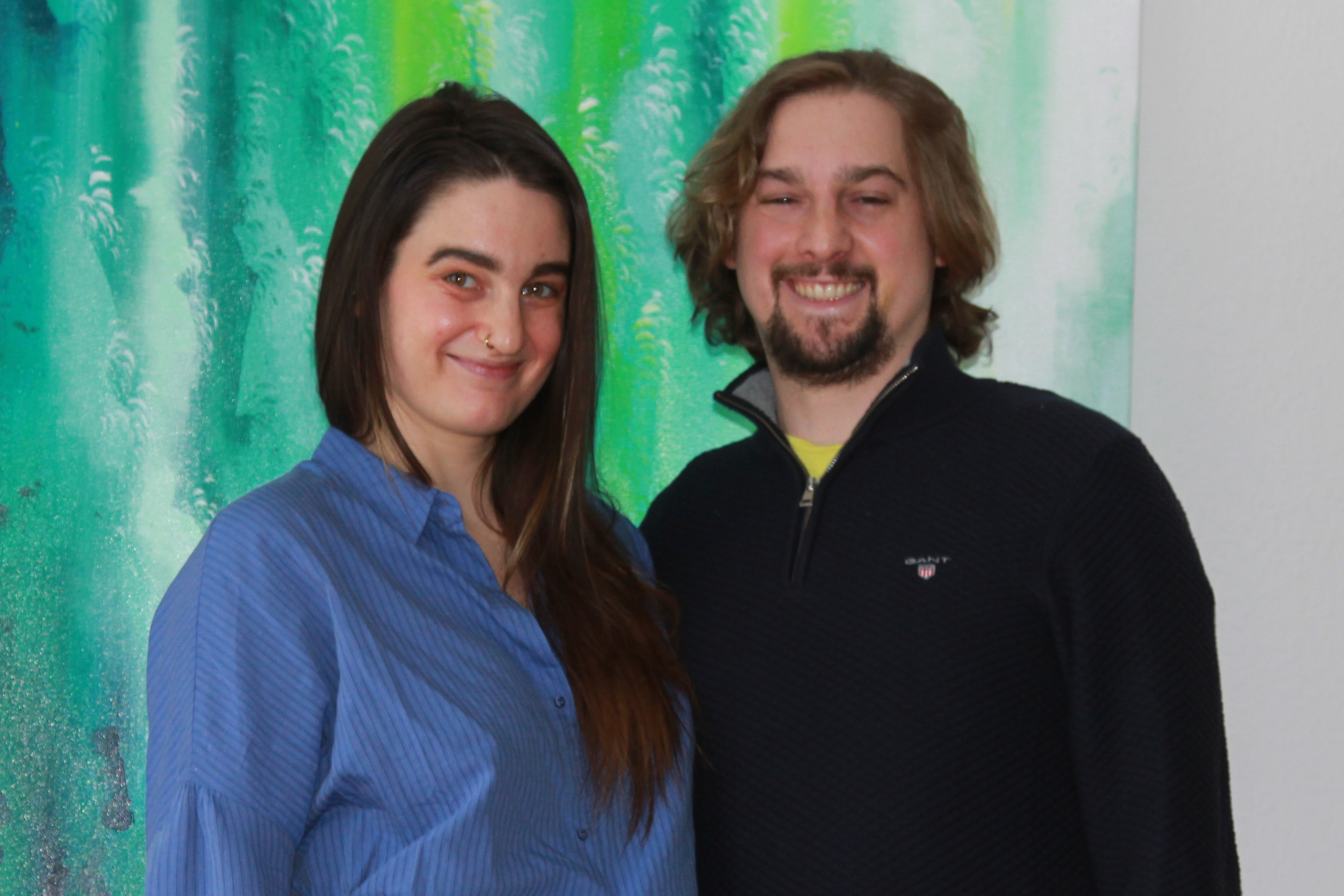 Frau und Mann stehen vor einer Wand und lächeln in die Kamera.